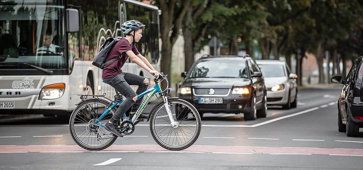 Sicherer Schulweg? Junge fährt auf dem Fahrrad über einen rot markierten Radweg an wartenden Autos vorbei.